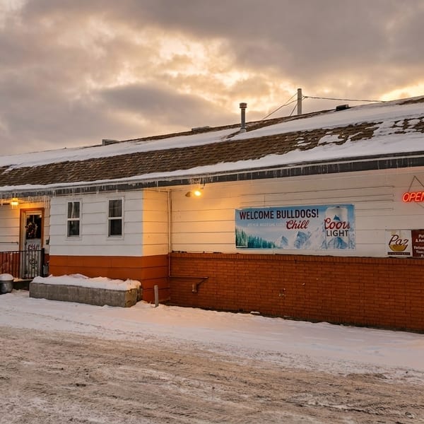 Paz Pub & Grill exterior in winter, with snow on the roof and ground under a cloudy sky.