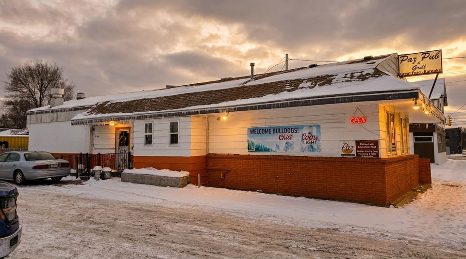 Paz Pub & Grill exterior in winter, with snow on the roof and ground under a cloudy sky.