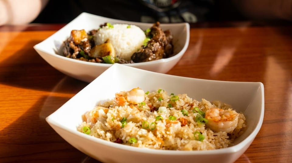 Two bowls of Asian cuisine: shrimp fried rice and beef with white rice and vegetables.