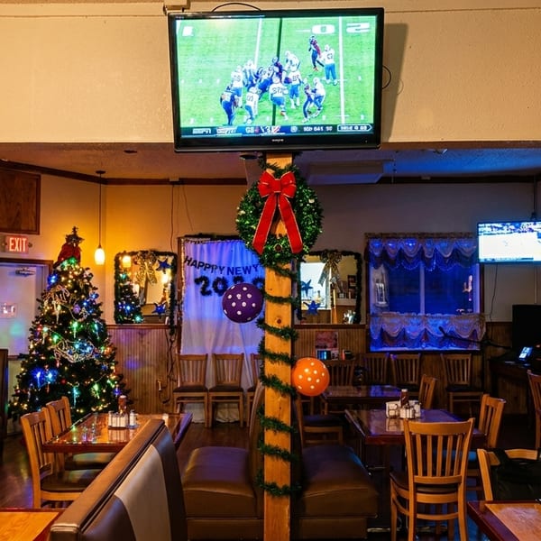 Restaurant interior decorated for New Year's, with Christmas trees, a bar, and TVs showing sports.