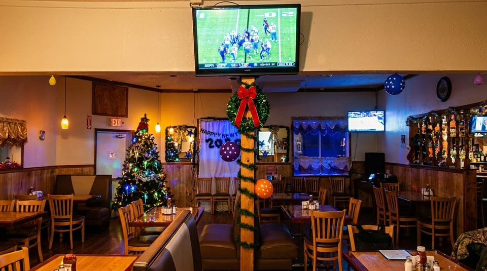 Restaurant interior decorated for New Year's, with Christmas trees, a bar, and TVs showing sports.